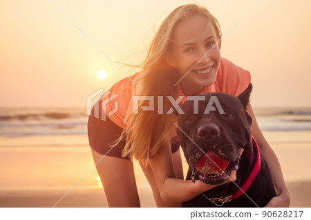 girl taking pictures photos of yourself on phone camera with their big dog Cane Corso black on indian ocean sea beach goa at sunset 90628217