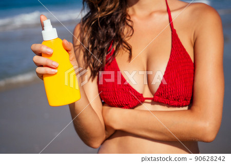 beautiful tanned female fitness big boobs model holding spf bottle 90628242