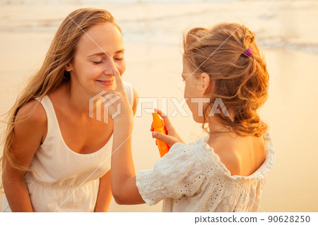 mother and teenager daughter using sunscreen on the beach 90628250
