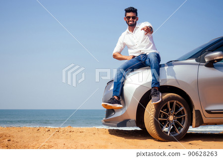 Indian businessman standing near car outdoors on sea beach summer good day.a man in a white shirt and snow-white smile rejoicing buying a new car enjoying a vacation by the ocean Indian businessman standing near car outdoors on sea beach summer good day.a man in a white shirt and snow-white smile rejoicing buying a new car enjoying a vacation by the ocean 90628263