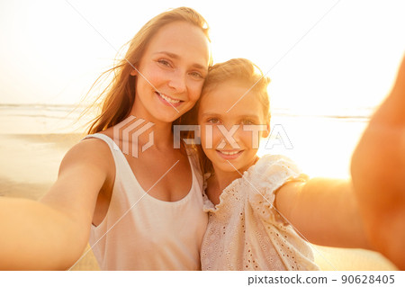 Happy stylishly mother and daughter taking selfie at sandy beach on a sunset.mothers Day.little girl blonde and beautiful woman taking pictures on the phone tourism abroad online video calling 90628405