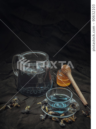Butterfly pea tea (Clitoria) or Organic blue anchan in Teapot and glass cup served with honey on Dark background. 90632103