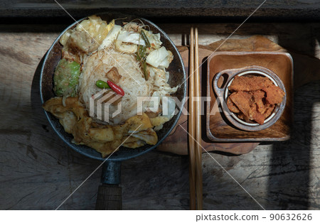 Stir fried rice vermicelli with pork dumplings, egg and vegetable in small steaming iron pot serve with crispy pork crackling or pork scratching. Stir fried rice vermicelli with pork dumplings, egg and vegetable in small steaming iron pot serve with crispy pork crackling or pork scratching. 90632626