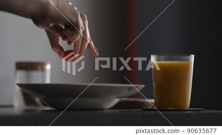 Adding cherry tomatoes to pasta in plate with glass of orange juice on countertop 90635677