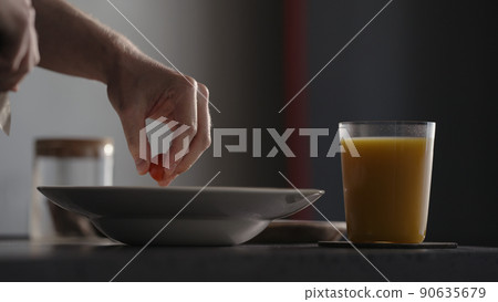 Adding cherry tomatoes to pasta in plate with glass of orange juice on countertop 90635679