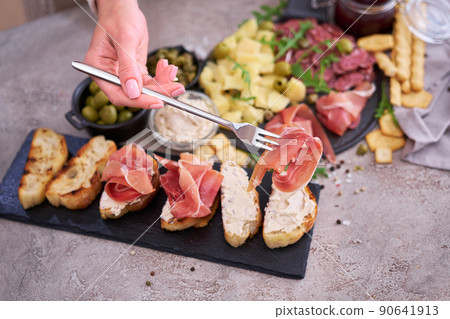 Woman holding piece of prosciutto ham on a fork standing at domestic kitchen Woman holding piece of prosciutto ham on a fork standing at domestic kitchen 90641913