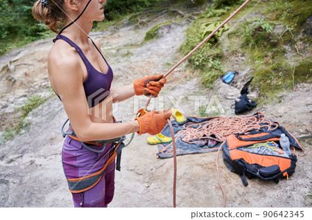 Close up of young female climber belaying leader during rock climbing outdoors, using rope, grigri, carabines and gloves. Concept of extreme sport and outdoor activity. Close up of young female climber belaying leader during rock climbing outdoors, using rope, grigri, carabines and gloves. Concept of extreme sport and outdoor activity. 90642345