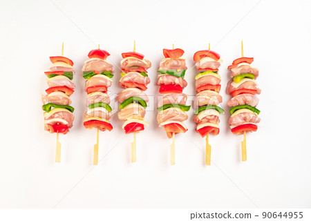 skewers of raw meat and vegetables.Frozen pieces of chicken skewers .Skewers with pieces of raw meat, red, yellow and green bell pepper, on white background. Close-up. 90644955