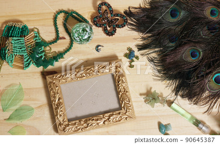 Green Jewelry and Peacock Feathers With Gold Picture Frame on Wooden Table Green Jewelry and Peacock Feathers With Gold Picture Frame on Wooden Table 90645387