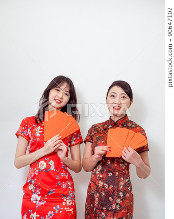 穿著傳統旗袍的年輕亞洲年輕及年長的女性,在白色背景前各自拿一疊的紅包袋,象徵財源廣進 90647102