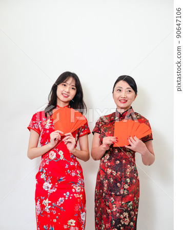 穿著傳統旗袍的年輕亞洲年輕及年長的女性,在白色背景前各自拿一疊的紅包袋,象徵財源廣進 90647106