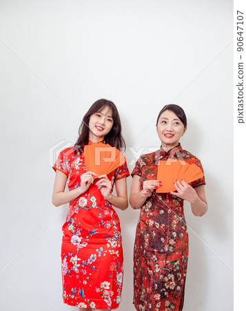 穿著傳統旗袍的年輕亞洲年輕及年長的女性,在白色背景前各自拿一疊的紅包袋,象徵財源廣進 90647107