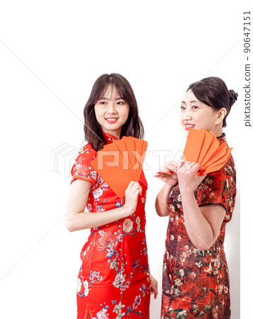 Young asian young and older women in traditional cheongsam holding stacks of red envelopes each in front of white background, symbolizing wealth Young asian young and older women in traditional cheongsam holding stacks of red envelopes each in front of white background, symbolizing wealth 90647151