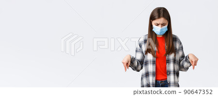 Coronavirus outbreak, leisure on quarantine, social distancing and emotions concept. Confused and unsure young woman in medical mask stare puzzled at something down, point bottom promo Coronavirus outbreak, leisure on quarantine, social distancing and emotions concept. Confused and unsure young woman in medical mask stare puzzled at something down, point bottom promo 90647352