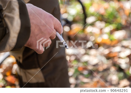 A smoking cigarette in a man's hand. Bad habit. The concept of the dangers of smoking and tobacco consumption with copy space for text A smoking cigarette in a man's hand. Bad habit. The concept of the dangers of smoking and tobacco consumption with copy space for text 90648291