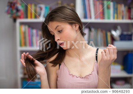 A teenager holds her long hair in her hand and looks at it. A teenager holds her long hair in her hand and looks at it. 90648293