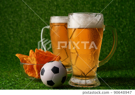 Two glasses of beer with soccer ball on the green grass background. Two glasses of beer with soccer ball on the green grass background. 90648947