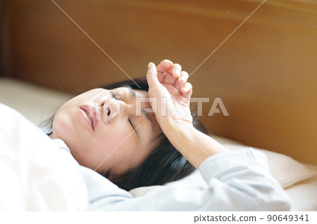 一個似乎難以入睡的中年女人，一個在床上把手放在額頭上的女人 90649341
