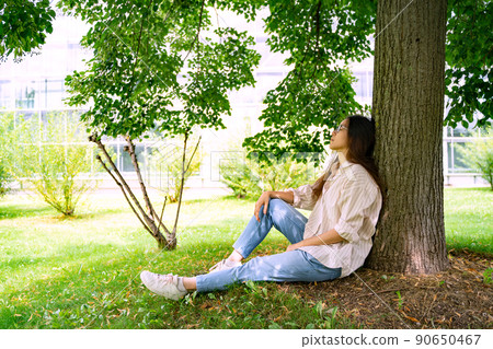 Young Vietnamese woman sitting relaxing in shadow under green tree on sunny day Young Vietnamese woman sitting relaxing in shadow under green tree on sunny day 90650467