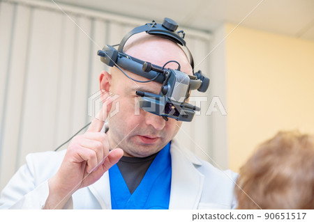 A male ophthalmologist checks the eyesight of an adult woman with a binocular ophthalmoscope 90651517