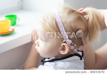 Mother fixing her daughter's cochlear implant hearing aid - deafness and diversity concept. Innovative technologies in treatment of deafness Mother fixing her daughter's cochlear implant hearing aid - deafness and diversity concept. Innovative technologies in treatment of deafness 90653670