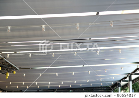 white textile ceiling of the sun shade canopy on the backyard terrace with string garlands with led bulbs suspended from the ceiling, decorative sun shade gazebo close up detail, nobody. 90654817