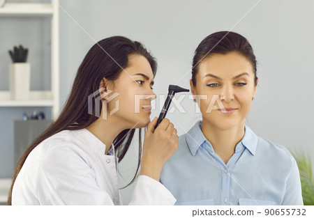 ENT doctor uses otoscope to examine young woman's ear during medical checkup in office ENT doctor uses otoscope to examine young woman's ear during medical checkup in office 90655732