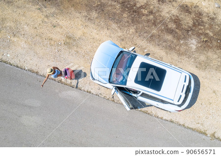 Woman with suitcase hitchhiking standing by broken down car with open hood at countryside road. Aerial, top, drone view 90656571
