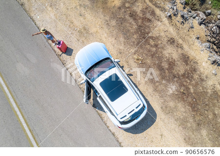 Woman with suitcase hitchhiking standing by broken down car with open hood at countryside road. Aerial, top, drone view 90656576