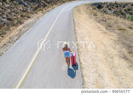 Woman with suitcase hitchhiking a car on the countryside road. Aerial, top, drone view 90656577