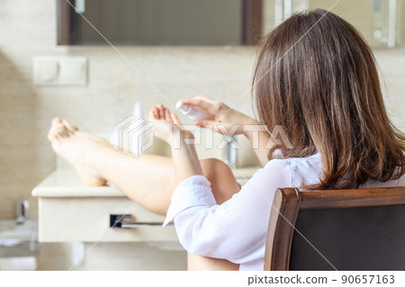 Woman in nightgown applying cream for protective and care dry skin legs sitting on armchair against mirror in bathroom. Woman in nightgown applying cream for protective and care dry skin legs sitting on armchair against mirror in bathroom. 90657163