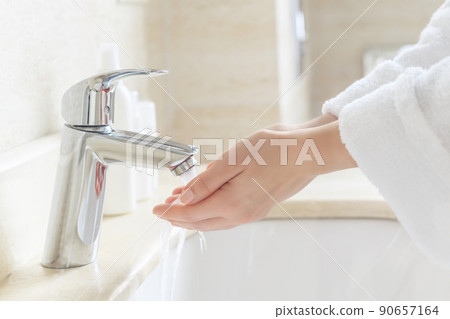 Woman in a robe washing hands in the bathroom under the water tap and stream or faucet without soap. Hygiene concept. Woman in a robe washing hands in the bathroom under the water tap and stream or faucet without soap. Hygiene concept. 90657164