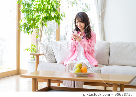 A young woman operating a smartphone in a room A young woman operating a smartphone in a room 90658733
