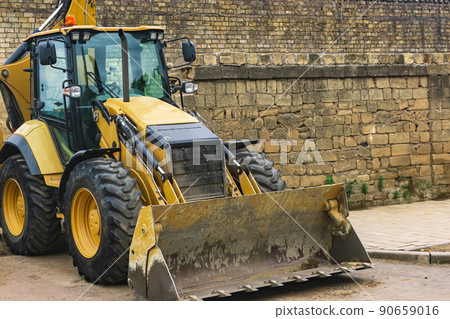 wheeled bucket loader next to a brick wall 90659016
