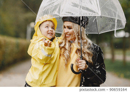 Family in a rainy park. Kids in a raincoats. Mother with child. Woman in a black coat. Family in a rainy park. Kids in a raincoats. Mother with child. Woman in a black coat. 90659164