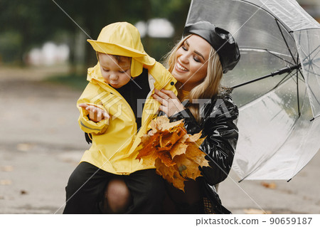 Family in a rainy park. Kids in a raincoats. Mother with child. Woman in a black coat. 90659187