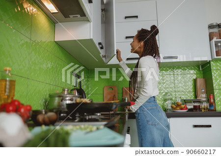 Side view of mixed-race beautiful woman opening kitchen cabinet, cooking concept Side view of mixed-race beautiful woman opening kitchen cabinet, cooking concept 90660217