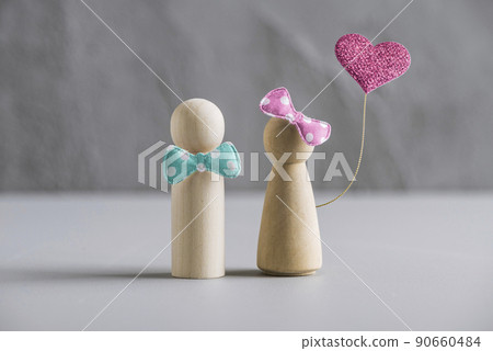 Wooden people man and woman with balloon in form of heart against the background of a gray concrete wall. The concept of Valentines day. Wooden people man and woman with balloon in form of heart against the background of a gray concrete wall. The concept of Valentines day. 90660484