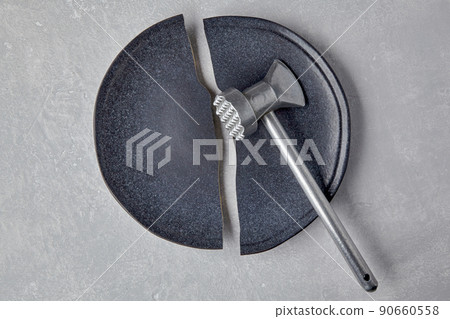 Broken ceramic plate and a kitchen hammer on a light concrete table Broken ceramic plate and a kitchen hammer on a light concrete table 90660558
