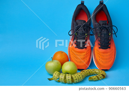 Orange sneakers, measuring tape and fruits apples and oranges on a blue background Orange sneakers, measuring tape and fruits apples and oranges on a blue background 90660563