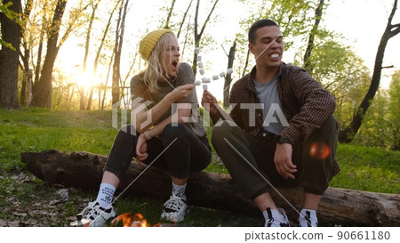 Camping and picnic concept. romantic couple frying marshmallow on fire in forest Letters on soks mean RUSSIAN WARSHIP GO FUCK 90661180