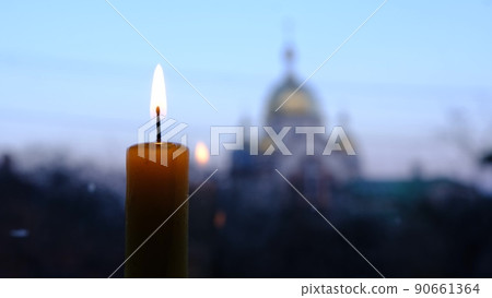 burning candle wit a blured church on background with the stained-glass windows Location 90661364