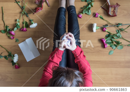Unhappy woman sitting on the floor among scattered flowers and reading letter. breakup. bad Valentine's day. concept. Top view Unhappy woman sitting on the floor among scattered flowers and reading letter. breakup. bad Valentine's day. concept. Top view 90661863