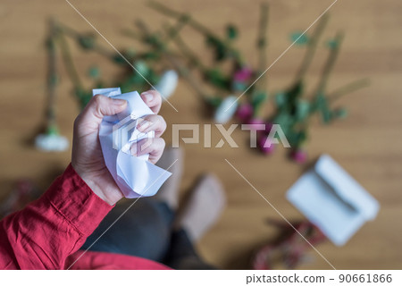 hand of woman with crumpled paper of letter among scattered flowers. Broken relationships in bad Valentine's day. concept. hand of woman with crumpled paper of letter among scattered flowers. Broken relationships in bad Valentine's day. concept. 90661866