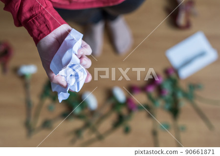 hand of woman with crumpled paper of letter among scattered flowers. Broken relationships in bad Valentine's day. concept. 90661871