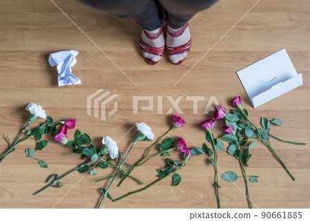 Top view of woman legs standing on the floor with crumpled paper of letter among scattered flowers. breakup. bad Valentine's day. concept. Top view of woman legs standing on the floor with crumpled paper of letter among scattered flowers. breakup. bad Valentine's day. concept. 90661885