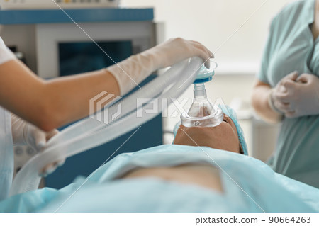 Close up hands of doctor anesthesiologist holding breathing mask on patient face during operation 90664263
