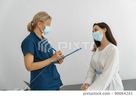 Doctor wearing protection mask against covid taking notes during consultation with patient Doctor wearing protection mask against covid taking notes during consultation with patient 90664281