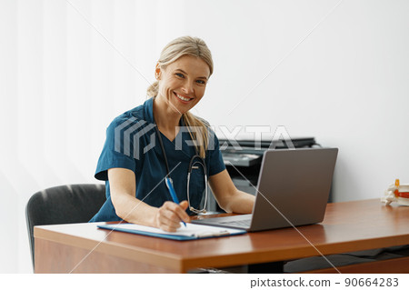 Female healthcare worker doing some paperwork and using laptop while working at doctor's office Female healthcare worker doing some paperwork and using laptop while working at doctor's office 90664283