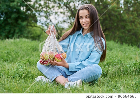 Young teenage female with apples sitting on the grass. 90664663